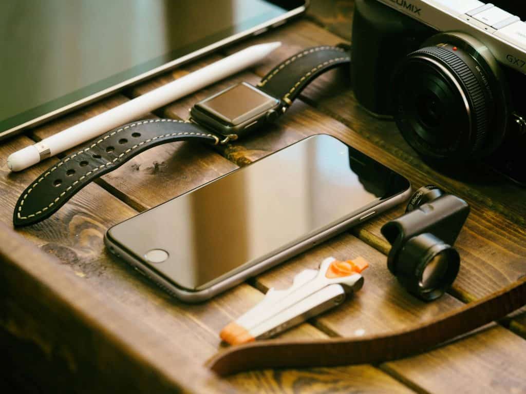 tablet, phone, camera, and a watch on a desk